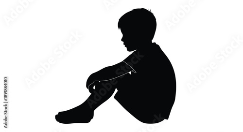 A young boy sitting with knees drawn up a dark silhouette