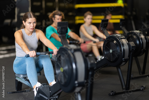 Tableau sur toile Young woman with sports leggings and a top does a cardio workout on a rowing machine