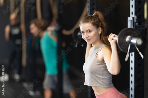 Woman is standing near a power rack with a barbell on her shoulders, she is doing squats and lunges on a Сrossfit classes. Young woman develops strength and endurance in functional training