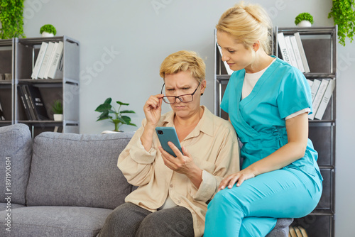 фотографія Senior woman using mobile phone with help of caregiver at home