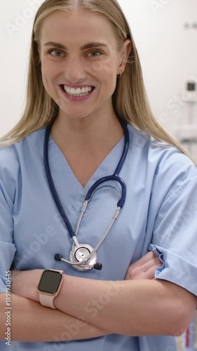 Vertical video: Smiling nurse widening grin as camera zooming in clinic with stethoscope in scrubs