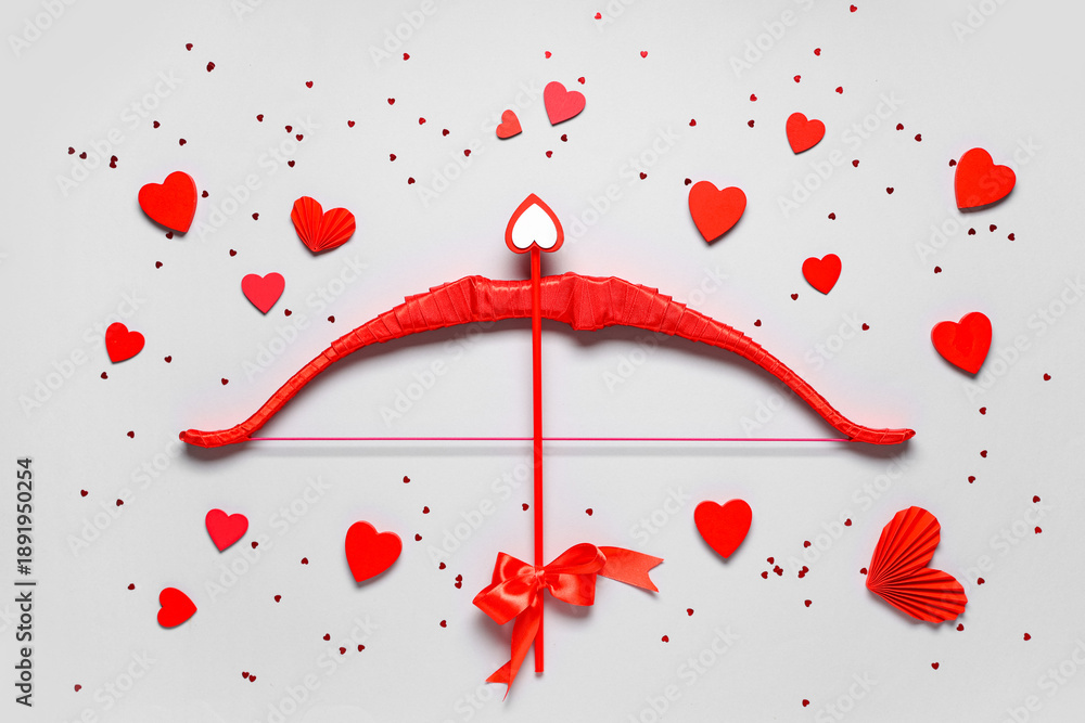Obraz premium Composition with red cupid's bow and paper hearts on grey background. Valentine's Day celebration