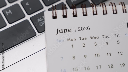 Close-up of a desk calendar showing June 2026 placed next to a laptop keyboard. Camera slowly rotates to the right, revealing clear date layout and calm monthly planning concept in a modern workspace.