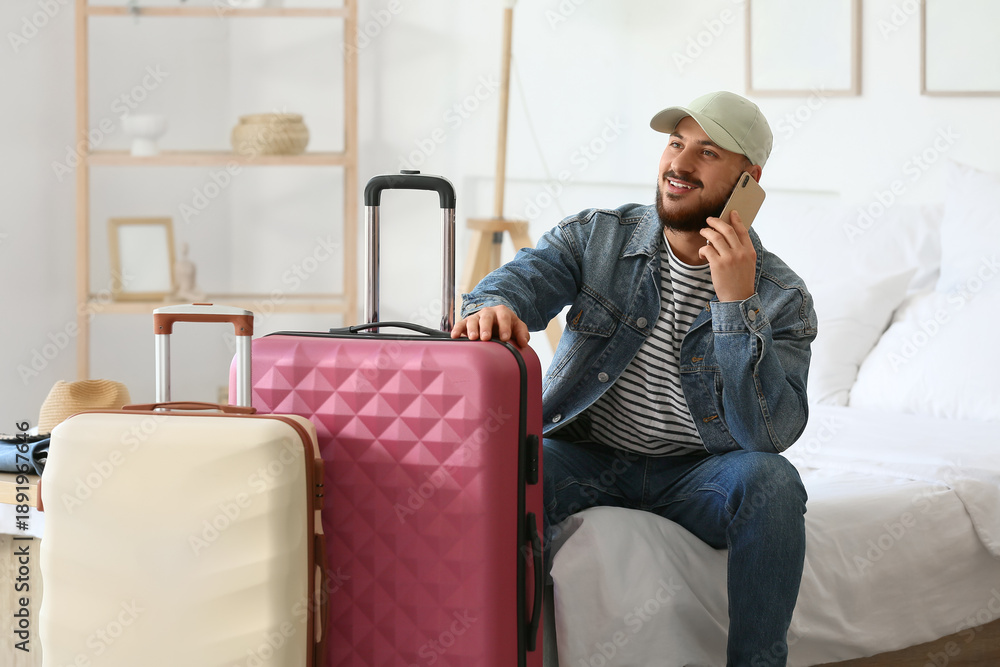 Fototapeta premium Male tourist with suitcases talking by mobile phone in hotel room