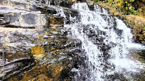 Natural clean water flows over geopark rocks which are the result of wood aging for thousands of years in the middle of a tropical forest which forms a terraced waterfall.