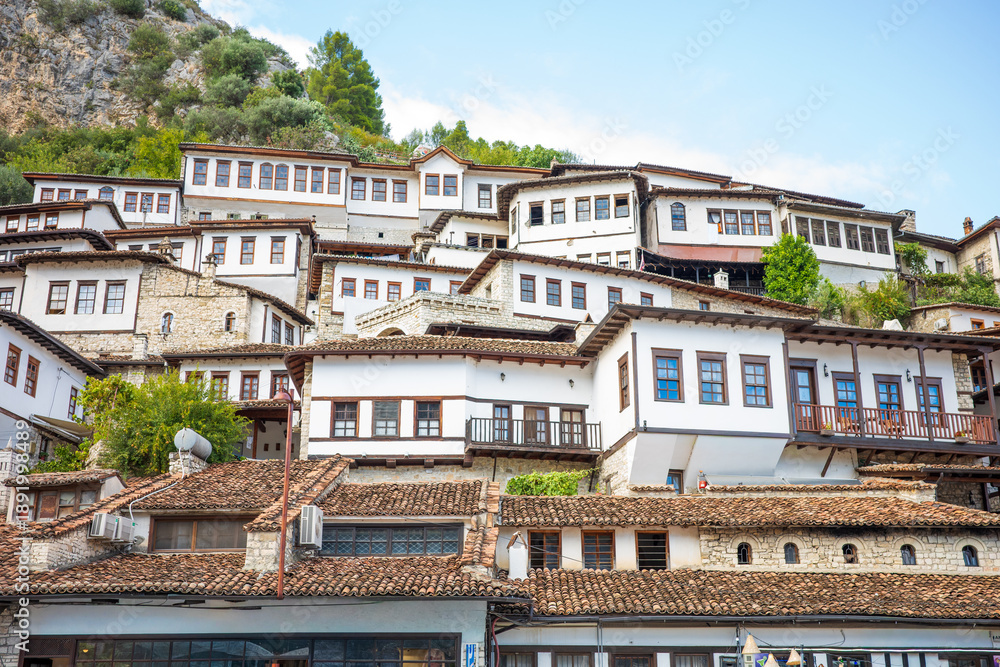 Obraz premium Rows of beautifully preserved white stone houses with wooden balconies and red tiled roofs rise along a lush green hillside, creating a stunning historic old town panorama