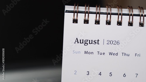 Close-up of a desk calendar on a laptop keyboard as a human finger points to a specific date in August 2026. Static camera highlights precise date indication and structured monthly planning in a mode