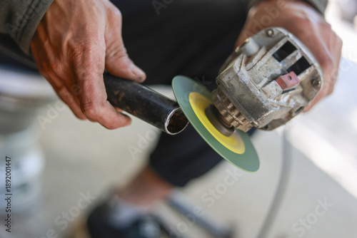 Fotografie Focused worker man using an angle grinder tool to grind metal pipe
