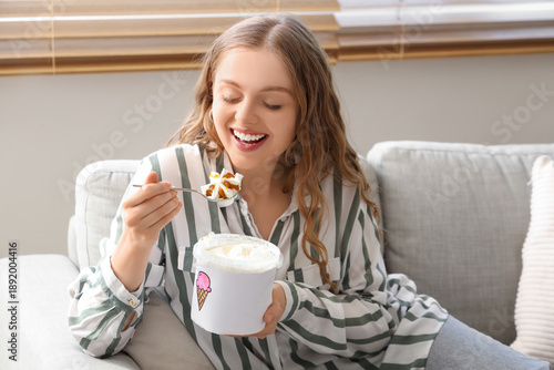 Foto Young woman with ice cream bucket sitting on sofa at home