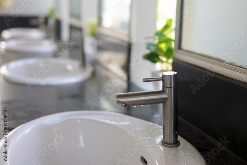 Clean modern bathroom interior design with row of white ceramic sinks and steel faucet. feeling of freshness and hygiene in public washroom or luxury spa