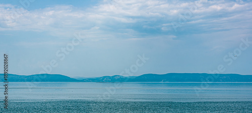 Photos Wide view of the Saint Lawrence River near Gaspésie, Quebec, with calm blue water, distant mountains and dramatic clouds, creating a serene coastal landscape with copy space