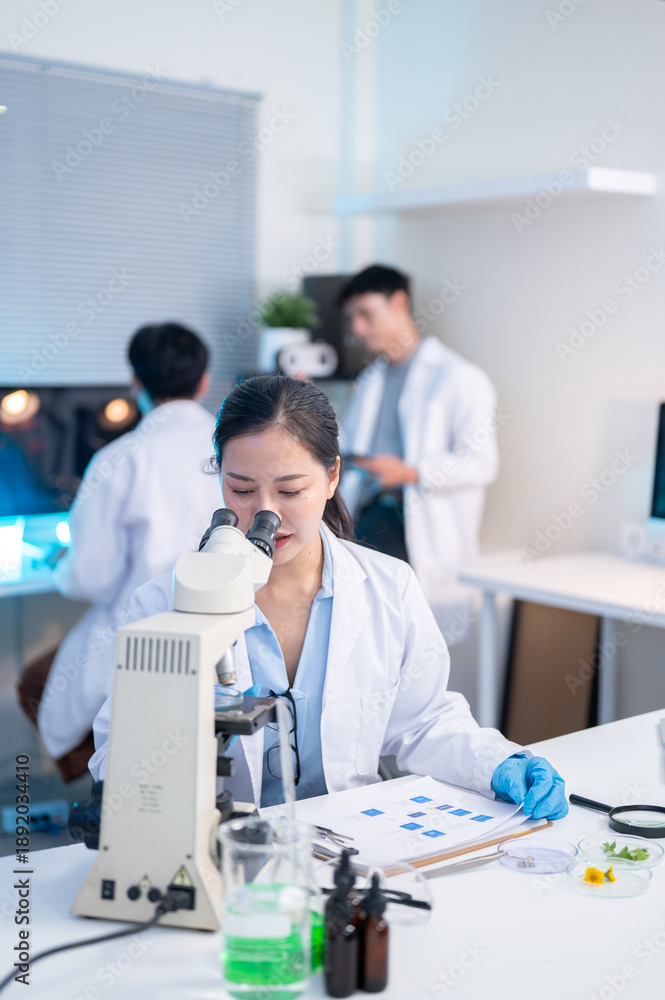 Obraz premium Woman scientist researcher using microscope looking at test sample and working with colleague in lab