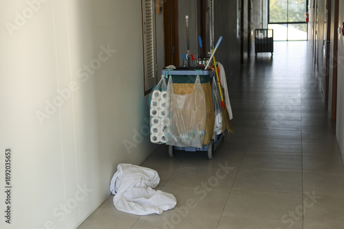 Quiet hotel hallway with janitorial cleaning cart and disposable garment on empty floor. long corridor shows lonely scene of abandoned maintenance work