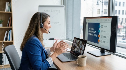 Businesswoman wearing a headset and blue blazer presents hybrid learning strategies on a monitor during a virtual meeting.