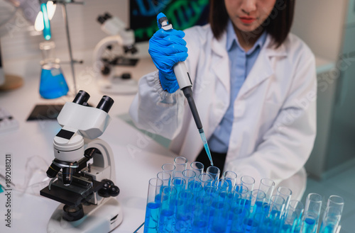 Female scientist pipetting liquid into multiple test tubes