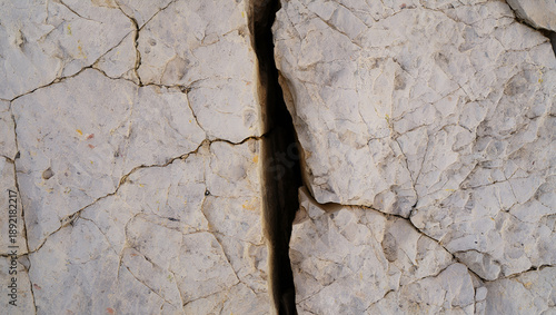 Broken plan fixed plan Close up of a large crack in a light gray textured rock surface