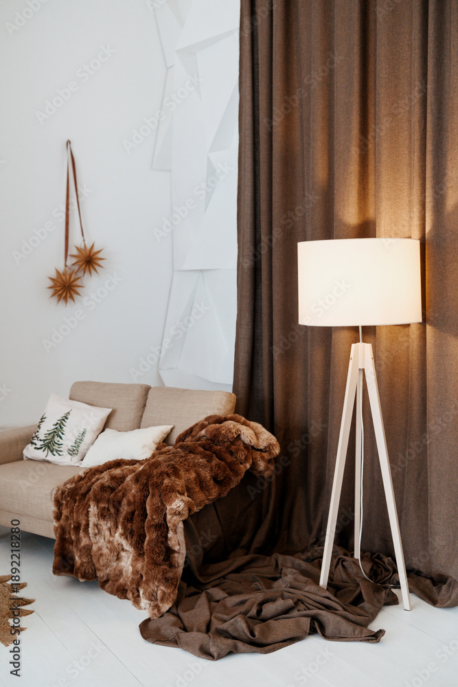 Naklejka premium Cozy sofa with plush blanket and floor lamp in a warm room setting with soft light.
