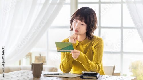 銀行の預金通帳を確認する女性, Woman checking a bank passbook at home