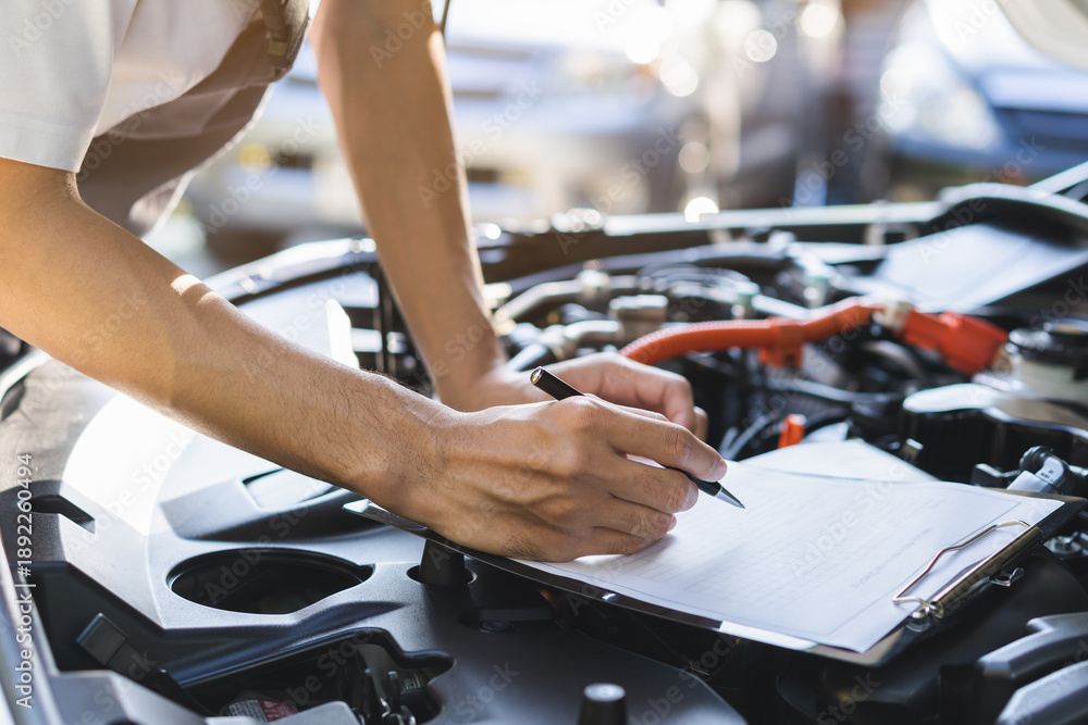 Fototapeta premium Auto check, car service shop concept. Automobile repairman writing job checklist on clipboard, mechanic checking engine to estimate repair machine, inspecting maintenance by engineer at vehicle garage