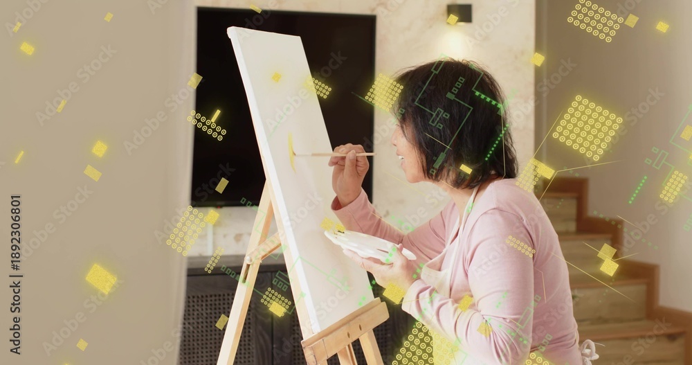Fototapeta premium Painting senior painter wearing pink top and apron in home with easel and palette, brush, graphics