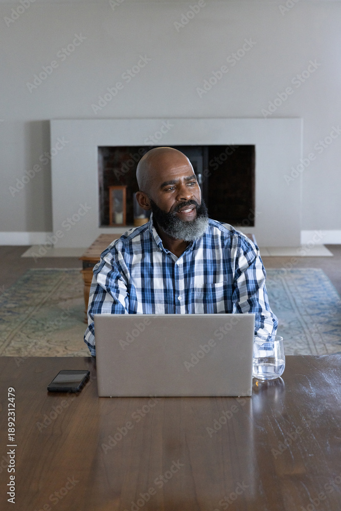 Fototapeta premium Senior african american man working on laptop with smartphone in living room at table