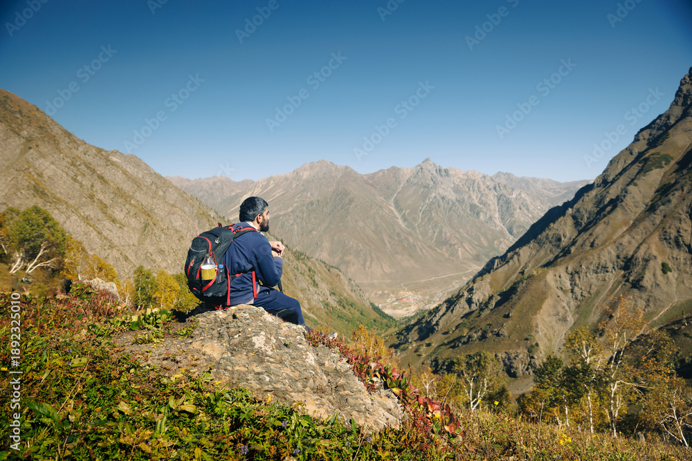 Fototapeta premium Male Hiker with Backpack Sitting on Rock Overlooking a remote Valley in the kashmir mountains