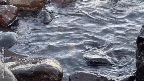 Calm ocean waves washing a rocky shore at dawn, soft pastel blue light before sunrise, minimal coastal scenery conveying freedom, travel lifestyle, nature balance, environment and relaxing seaside mor