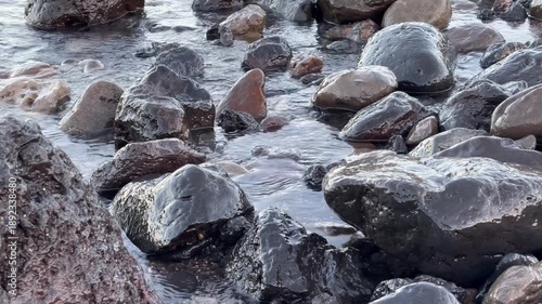 Calm ocean waves washing a rocky shore at dawn, soft pastel blue light before sunrise, minimal coastal scenery conveying freedom, travel lifestyle, nature balance, environment and relaxing seaside mor