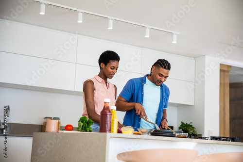 Diverse couple cooking vegetables in frying pan on kitchen island with tomato and cutting board