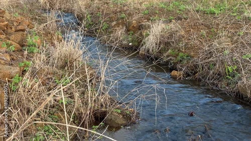 Narrow Stream Flowing Through Dry Grass and Rocks in a Natural Landscape