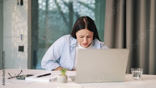 Woman experiencing sudden, sharp abdominal pain while concentrating on laptop. Face reveals immense discomfort and suffering, indicating health problem or illness. Feeling unwell and distressed.