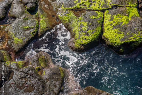 Waves Crashing Against Moss-Covered Coastal Rocks, Top View