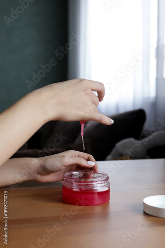Close-up of a woman's hands in the process of skin care - a girl applies a pink scrub, gently cleansing and exfoliating the skin. The treatment symbolizes home spa care, self-care, beauty and health