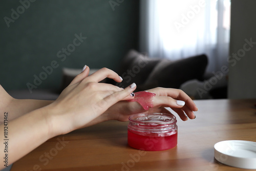 Close-up of a woman's hands in the process of skin care - a girl applies a pink scrub, gently cleansing and exfoliating the skin. The treatment symbolizes home spa care, self-care, beauty and health
