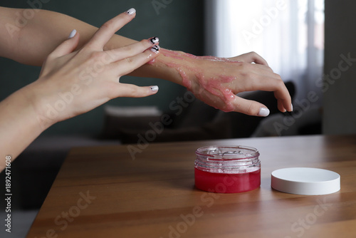 Close-up of a woman's hands in the process of skin care - a girl applies a pink scrub, gently cleansing and exfoliating the skin. The treatment symbolizes home spa care, self-care, beauty and health
