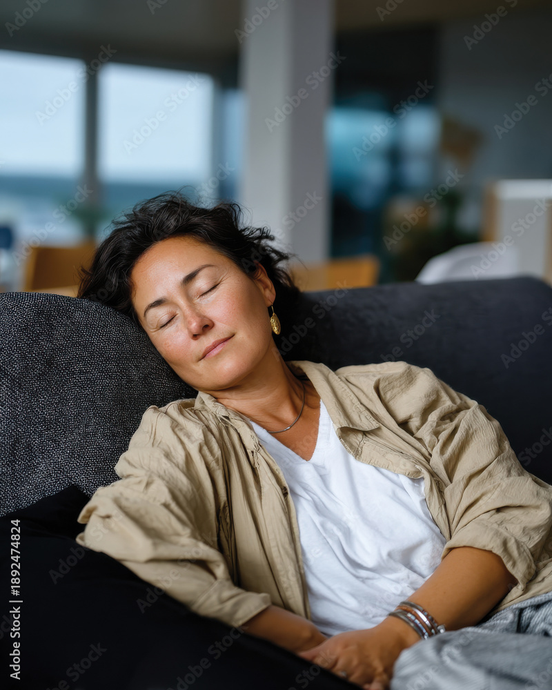 Obraz premium A relaxed woman enjoys a restorative moment, napping on a cozy sofa, embodying tranquility and the necessity of self-care in a busy life.