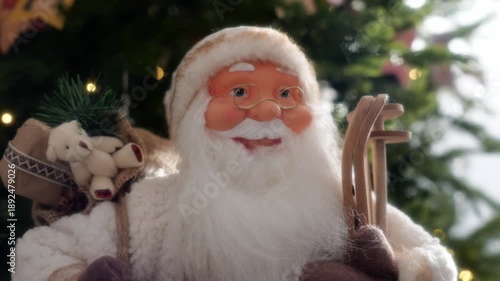 A charming Santa Claus figurine with a sled and teddy bear is set against a beautifully lit Christmas tree, creating a festive and heartwarming holiday atmosphere.