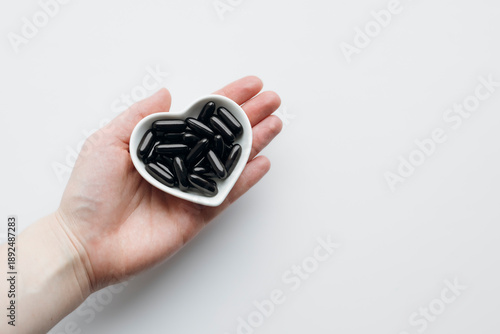 Hand holding a heart-shaped plate filled with iron capsules on a white.