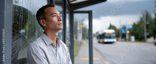 Thoughtful man waiting at rainy bus stop with blurred city street and approaching bus in background