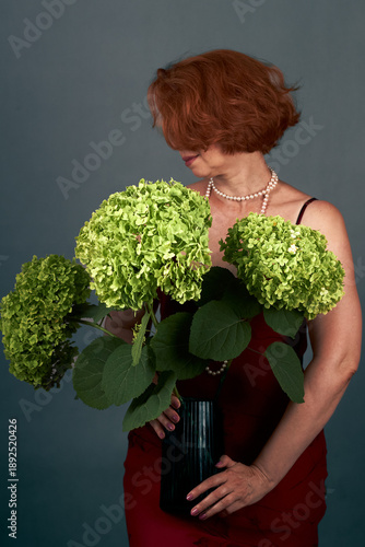 Elegant woman holding green hydrangeas in vase against muted studio background portrait