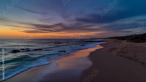 Serene ocean waves gently kiss sandy shore under vibrant sunset sky with dramatic pink and orange clouds reflecting on wet sand and calm water creating a peaceful coastal atmosphere perfect for