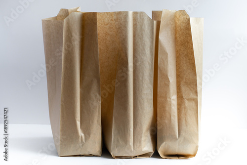 three brown paper bags are placed next to each other on smooth surface. they have simple design. light reflects off their surfaces. concept delivery. close up.