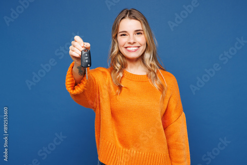 Fotografie Young happy Caucasian woman she wear yellow sweater casual clothes hold in hand car key fob keyless system stretch arm to camera isolated on plain blue background studio portrait