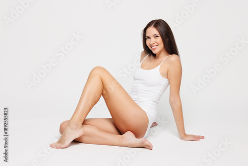 Foto Full length side view young woman with slim fit body perfect skin wear lingerie underwear sit with long legs extended isolated on plain solid white background studio portrait