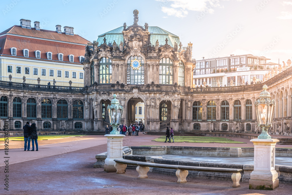 Obraz premium Visitors walk around the Zwinger Palace in Dresden, Germany. The majestic buildings stand tall under the winter sun as people enjoy the festive atmosphere during Christmas time.