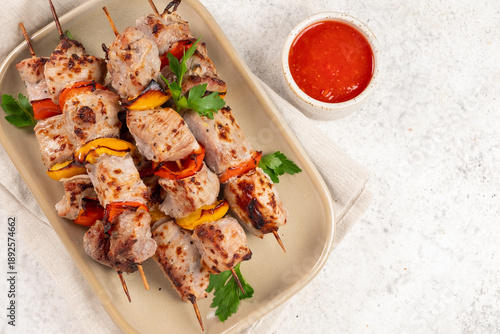 Grilled meat skewers served with vegetables and sauce on a plate with green herbs on a light table © azurita