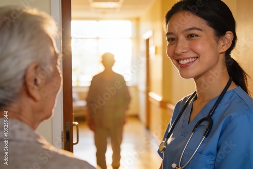 Young asian nurse wearing blue scrubs smiling while communicating with a senior patient in a brightly lit hospital corridor for healthcare and compassion concept.