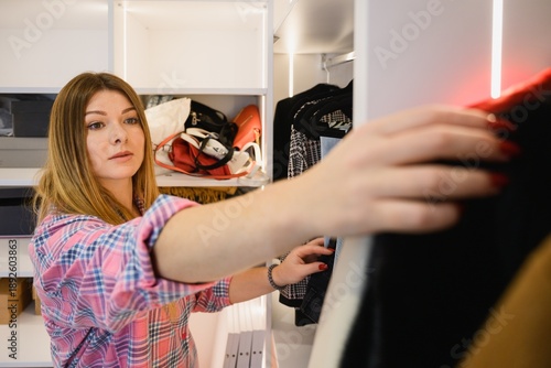 Young woman selecting clothes in a home wardrobe. Casual lifestyle moment, fashion choice, organization of clothing in a bright dressing room.
