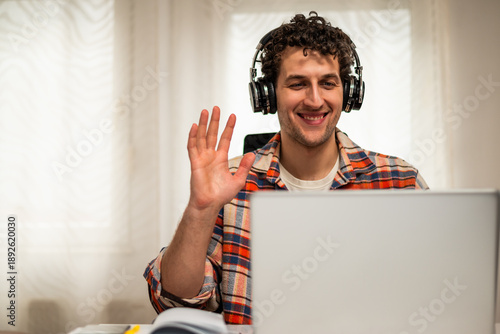 Wallpaper Mural Smiling young man talking and waving during video call on laptop while sitting at his comfortable home.	 Torontodigital.ca