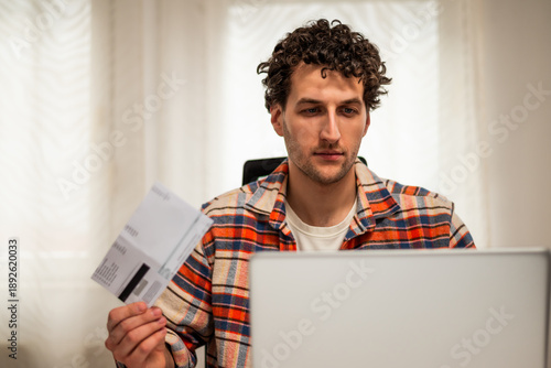 Wallpaper Mural Focused young man using laptop and credit card to pay bills online, managing his finances and carefully reviewing expenses while sitting in his living room. Torontodigital.ca